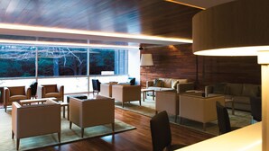 A modern living room with wooden floors, a large window with a view of trees, and a mix of sofas and armchairs.
