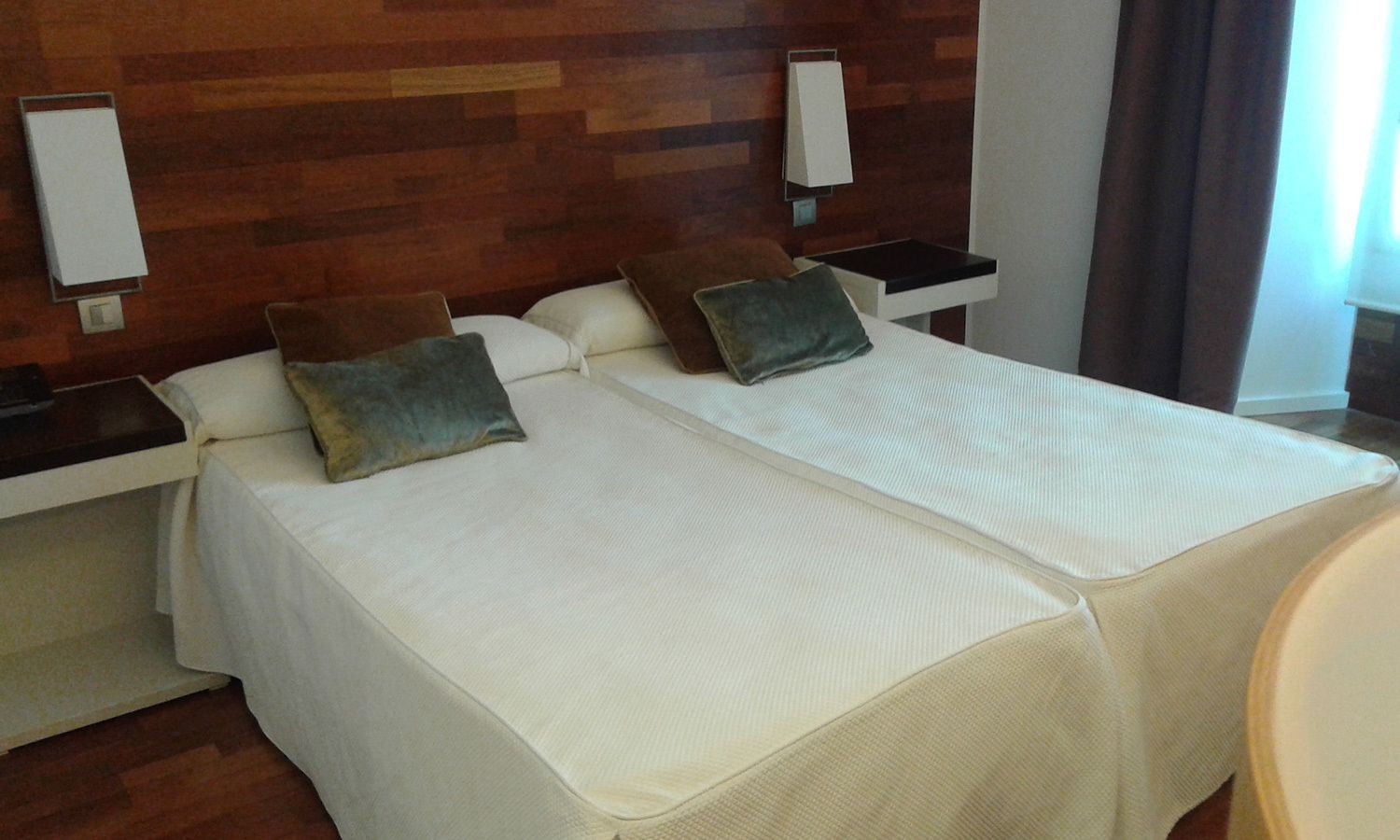 Habitación de hotel con dos camas, cada una con almohada y mesita de noche.