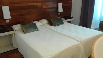Habitación de hotel con dos camas, cada una con almohada y mesita de noche.