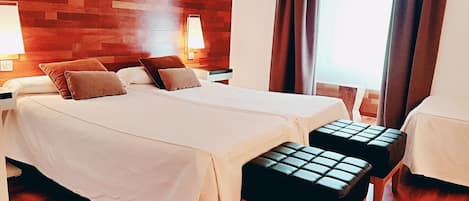 A hotel room with a wooden wall, a bed with white linens, two pillows, a bench, a nightstand, and a lamp.
