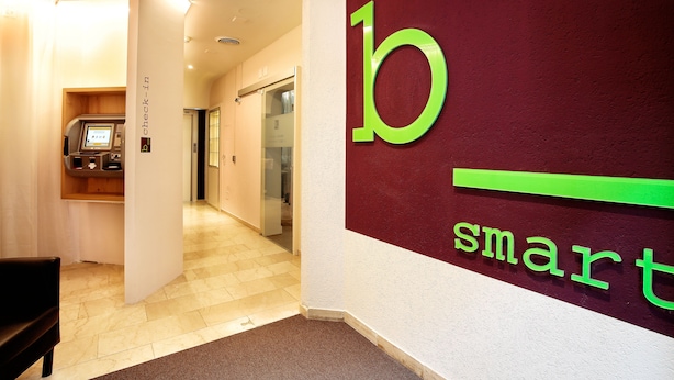 A check-in area with a 'b smart' sign, a reception desk, and a glass door leading to a hallway. - b_smart motel Basel (Basel)