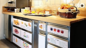 A breakfast bar with a coffee machine, a fruit display, and a menu board. - b_smart motel Basel (Basel)