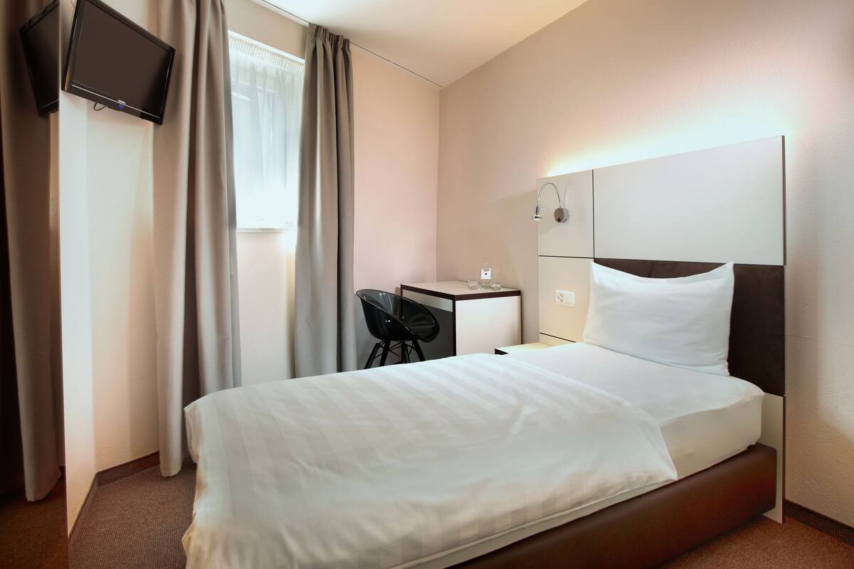 A hotel room with a bed, a desk, a chair, a TV, and a window with curtains.