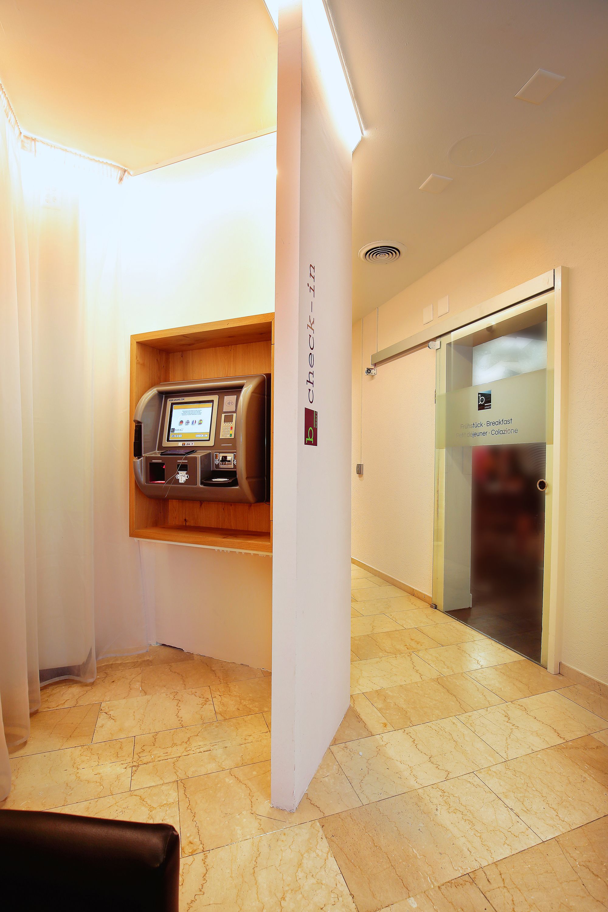 A check-in kiosk, a reception area with a glass door, and a tiled floor.