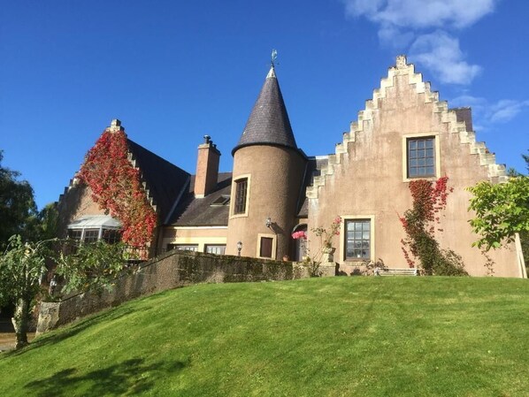 Un grand bâtiment historique, doté d’une tour imposante, d’un toit à forte pente et d’une pelouse bien entretenue.