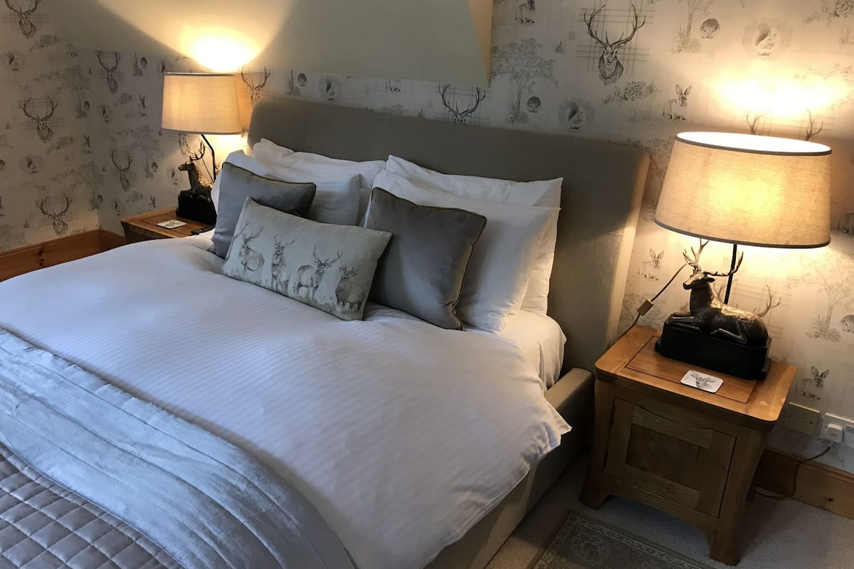 Una cama bien hecha con un cabecero gris, dos mesitas de noche con lámparas, y un papel tapiz estampado con motivos de animales.