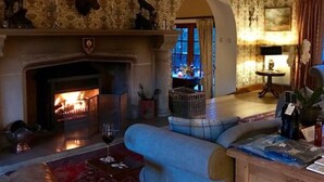 A cozy living room with a fireplace, patterned wallpaper, and antler decorations. - Highland Bear Lodge & Woodland Bear Huts (Inverness)