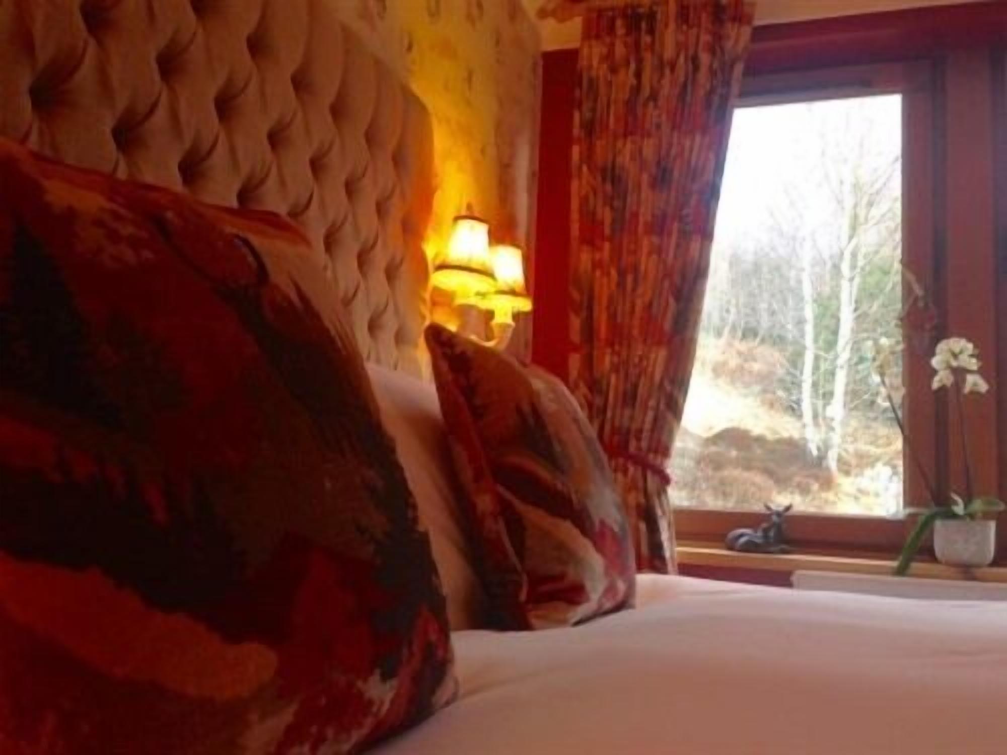 A bedroom with a large bed, a window with curtains, and a lamp on the wall.