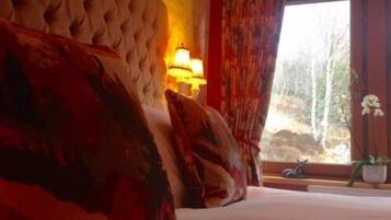 A bedroom with a large bed, a window with curtains, and a lamp on the wall.