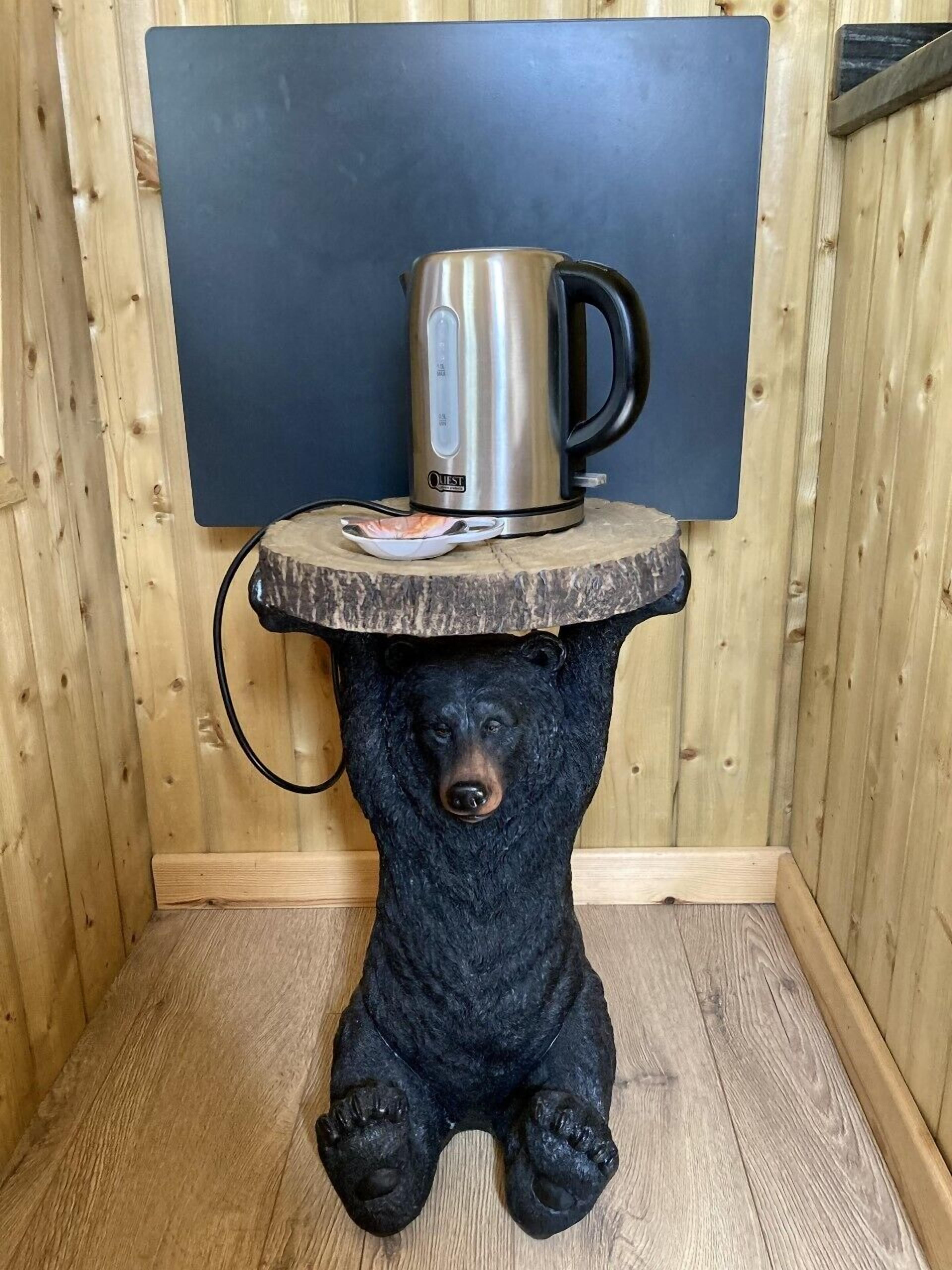 Una estatua de oso con una tetera en la cabeza, colocada sobre una mesa de madera frente a una pared de madera.