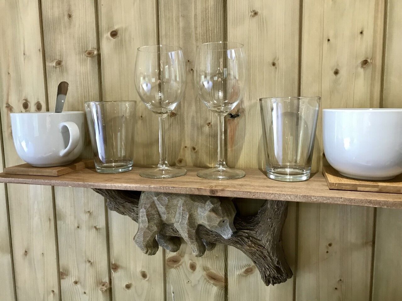 Une étagère en bois sur laquelle sont disposés divers objets en verre et un bol blanc.