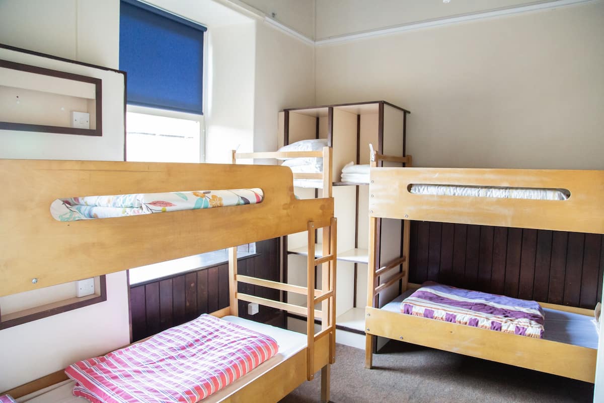 A bunk bed room with wooden frames and a window with blinds.