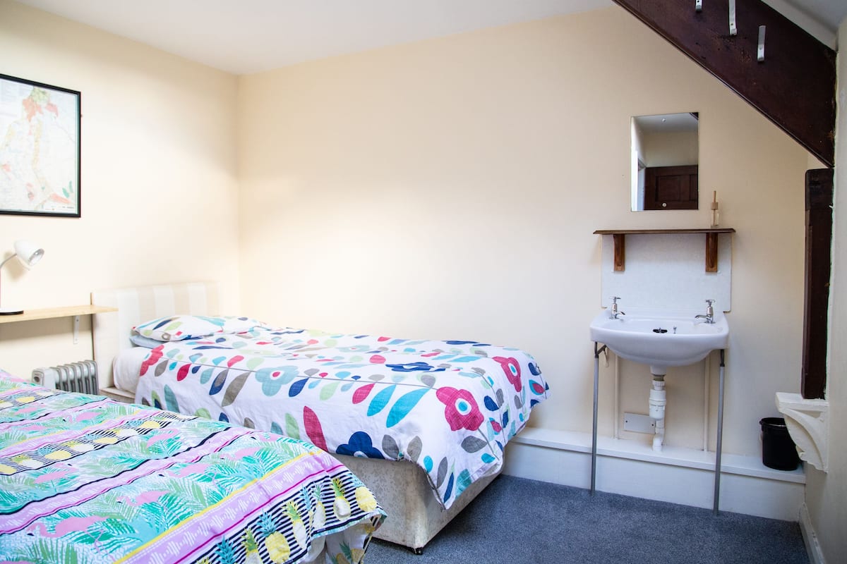 A bedroom with two beds, a window, a radiator, a sink, and a wooden staircase.