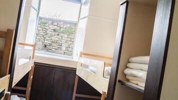 Un dormitorio con literas, una ventana con vistas a un muro de piedra y un estante con toallas dobladas.