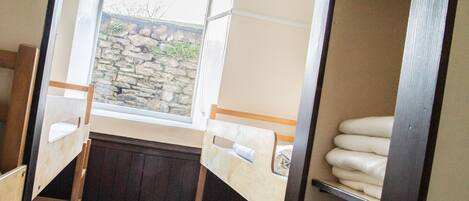 A dormitory room with bunk beds, a window with a stone wall view, and a shelf with folded towels.