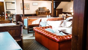 A cozy room with a wooden bench, a red leather sofa, a dining table, and a kitchen area in the background. - Kirkby Stephen Hostel (Kirkby Stephen)