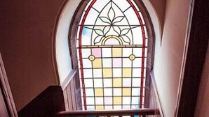 A staircase with a wooden handrail, a green patterned floor, and a stained glass window with a floral design. - Kirkby Stephen Hostel (Kirkby Stephen)
