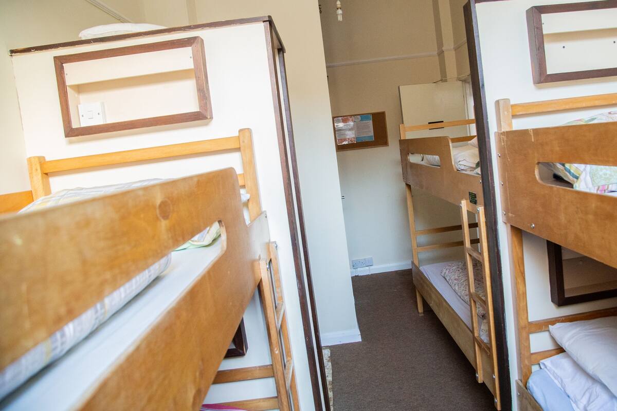 A dormitory room with bunk beds, a bulletin board, and a carpeted floor.