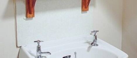 A bathroom with a white sink, two faucets, and a wooden shelf above it.