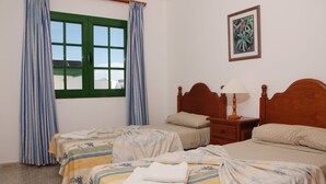 Habitación de hotel con dos camas, una ventana con cortinas, una mesita de noche con lámpara y un cuadro enmarcado en la pared.