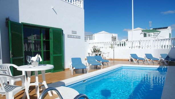 Zona de piscina con sillones reclinables, una mesa y un cartel que dice "Villa Playa El Salado".