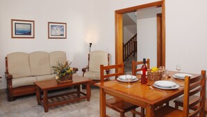 Un comedor con una mesa de madera preparada para dos personas, un sofá y dos cuadros en la pared.
