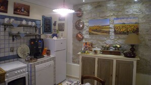 Una cocina equipada con estufa, horno y lavavajillas, además de un comedor con mesa y sillas. Se observan estanterías empotradas con vajilla y un menú en una pizarra.