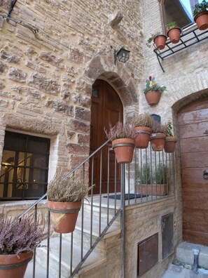 A stone building with a wooden door and multiple hanging flower pots. - B&B A Casa delle Fate (Assisi)