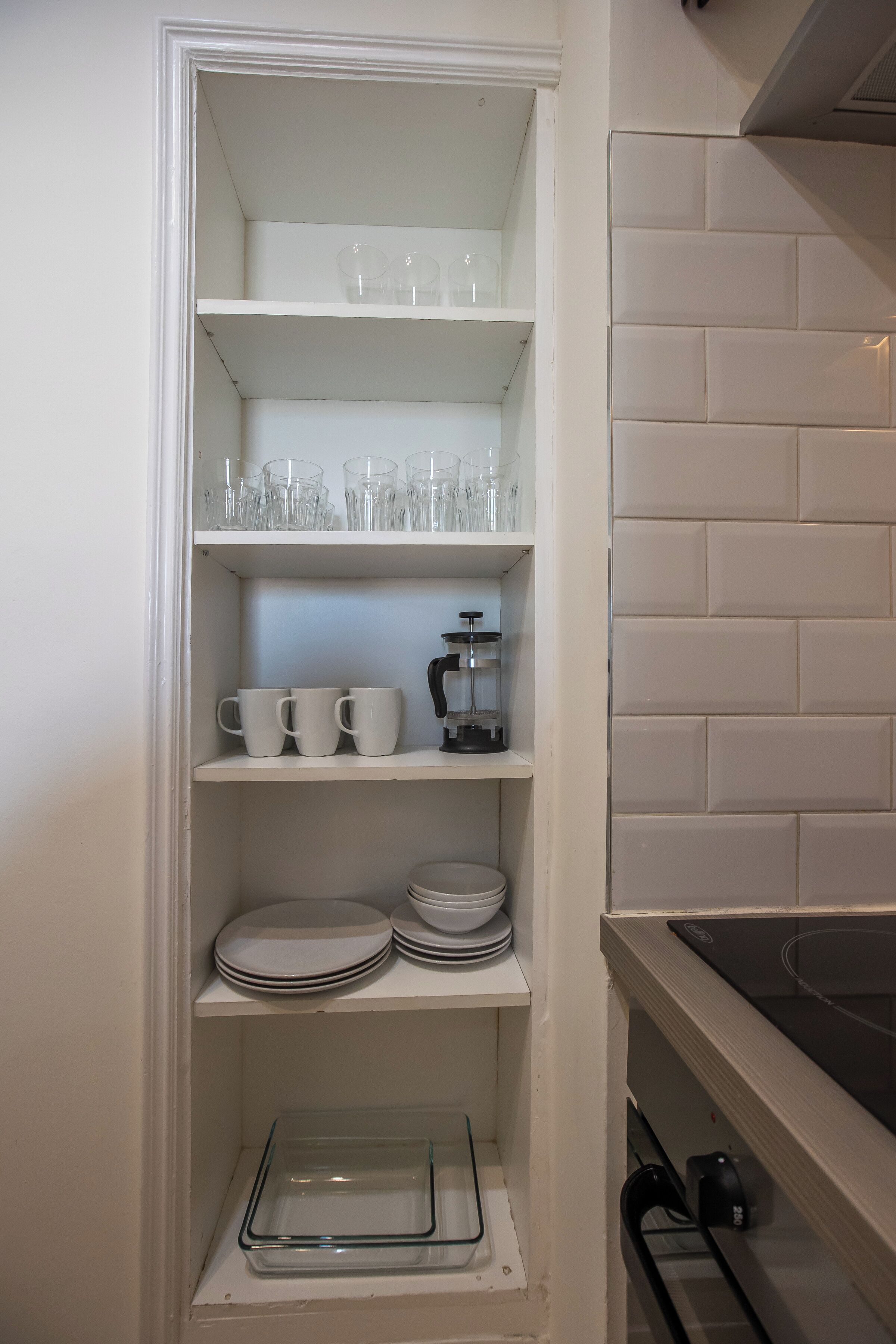 A kitchen with white cabinets, a stove, and shelves with dishes and glasses.