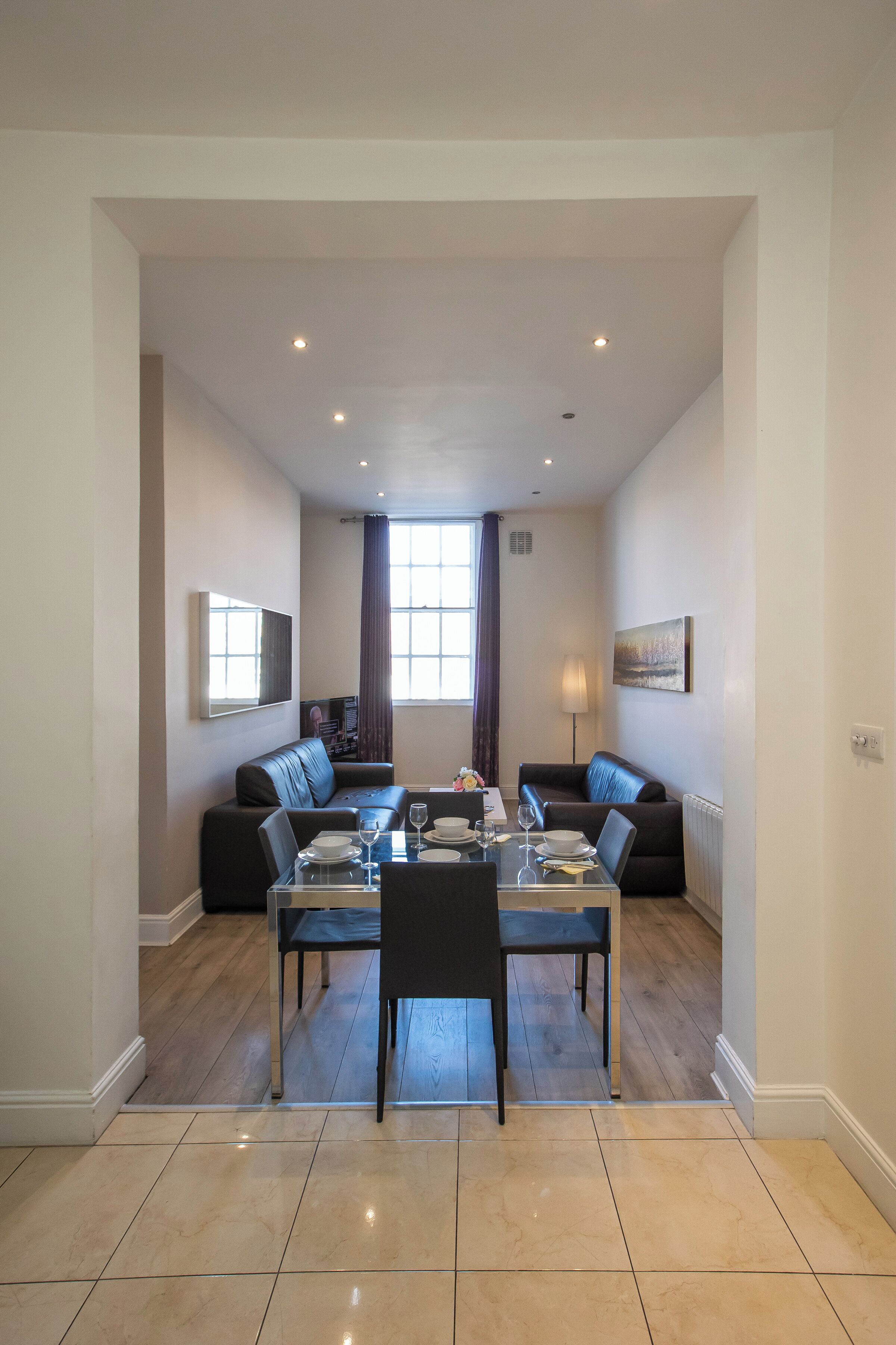 A dining area with a table set for four, two sofas, and a television mounted on the wall.