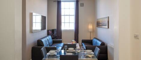 A dining area with a table set for four, two sofas, and a television mounted on the wall.