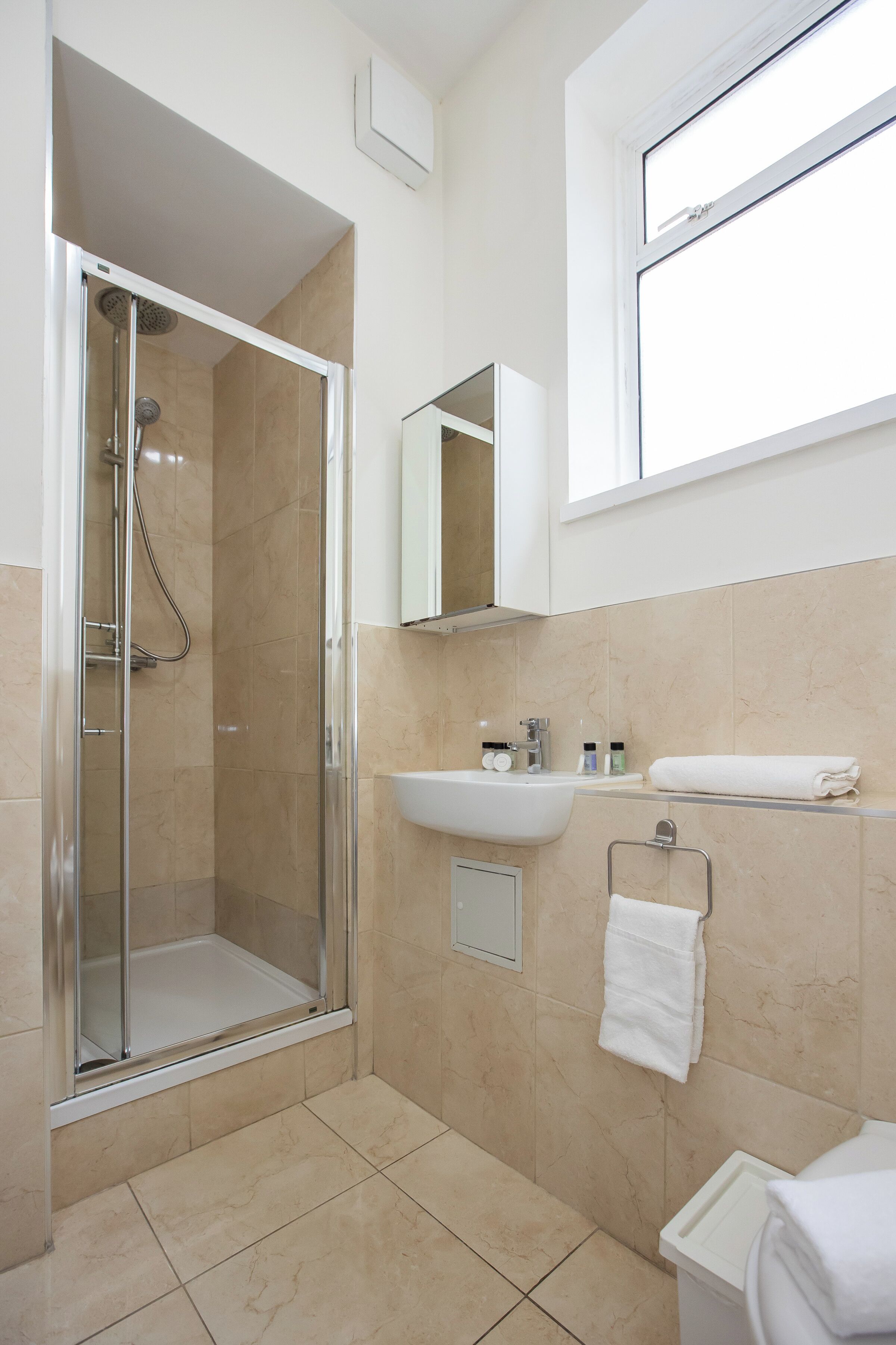 A modern bathroom with a glass-enclosed shower, a sink with a mirror above, and a window providing natural light.