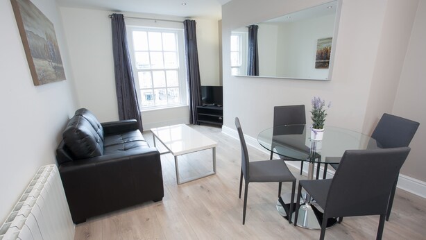 A modern living room with a black leather sofa, a glass coffee table, and a dining area with a glass table and chairs. - Temple Bar Wellington Quay Apartments (Dublin)