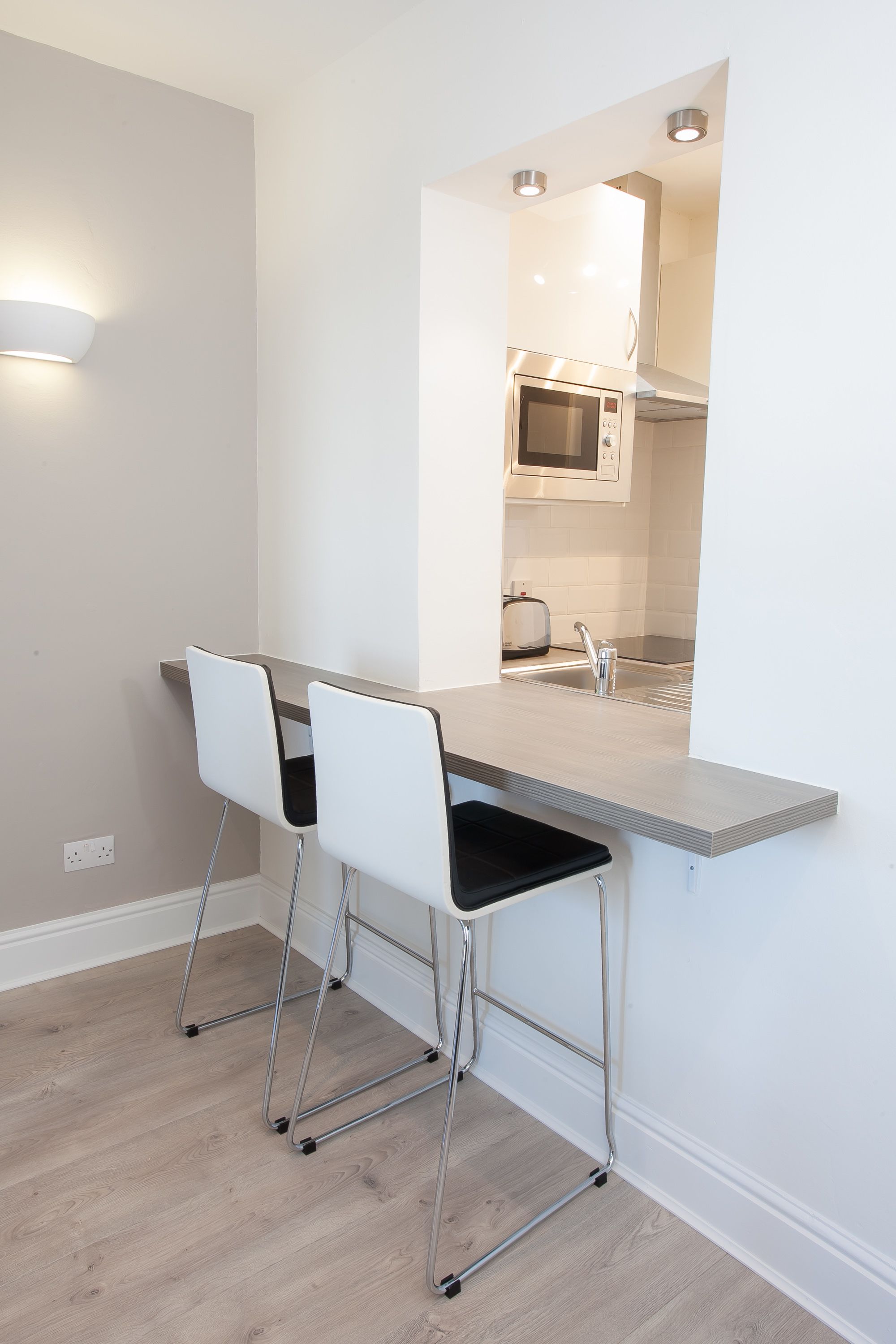 A modern kitchen with a built-in microwave, a sink, and a bar counter with two white bar stools.