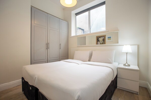 Un dormitorio con cama, mesita de noche, ventana y armario.