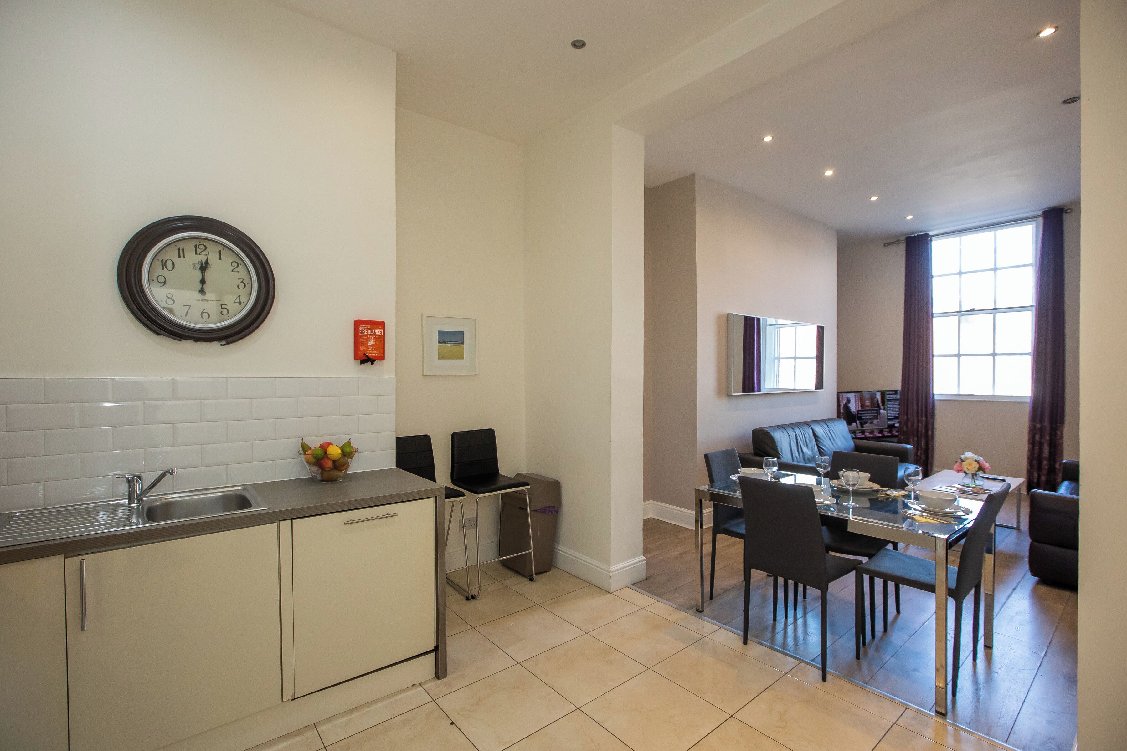 A modern kitchen with a sink, a clock, and a dining area with chairs and a table.