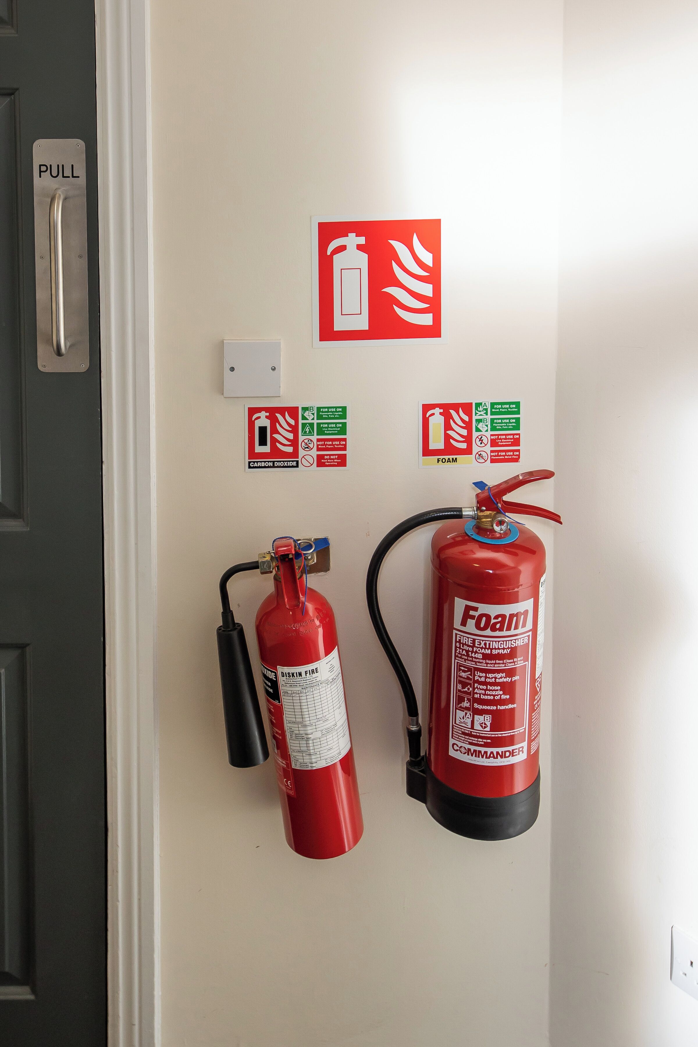 Ein an der Wand befestigter Feuerlöscher mit Zughebel und einem roten Schaumlöscher mit den Aufschriften "Foam" und "Commander" darunter.