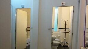 Un couloir menant à une salle de bain équipée d’une douche, de toilettes et d’un lavabo.