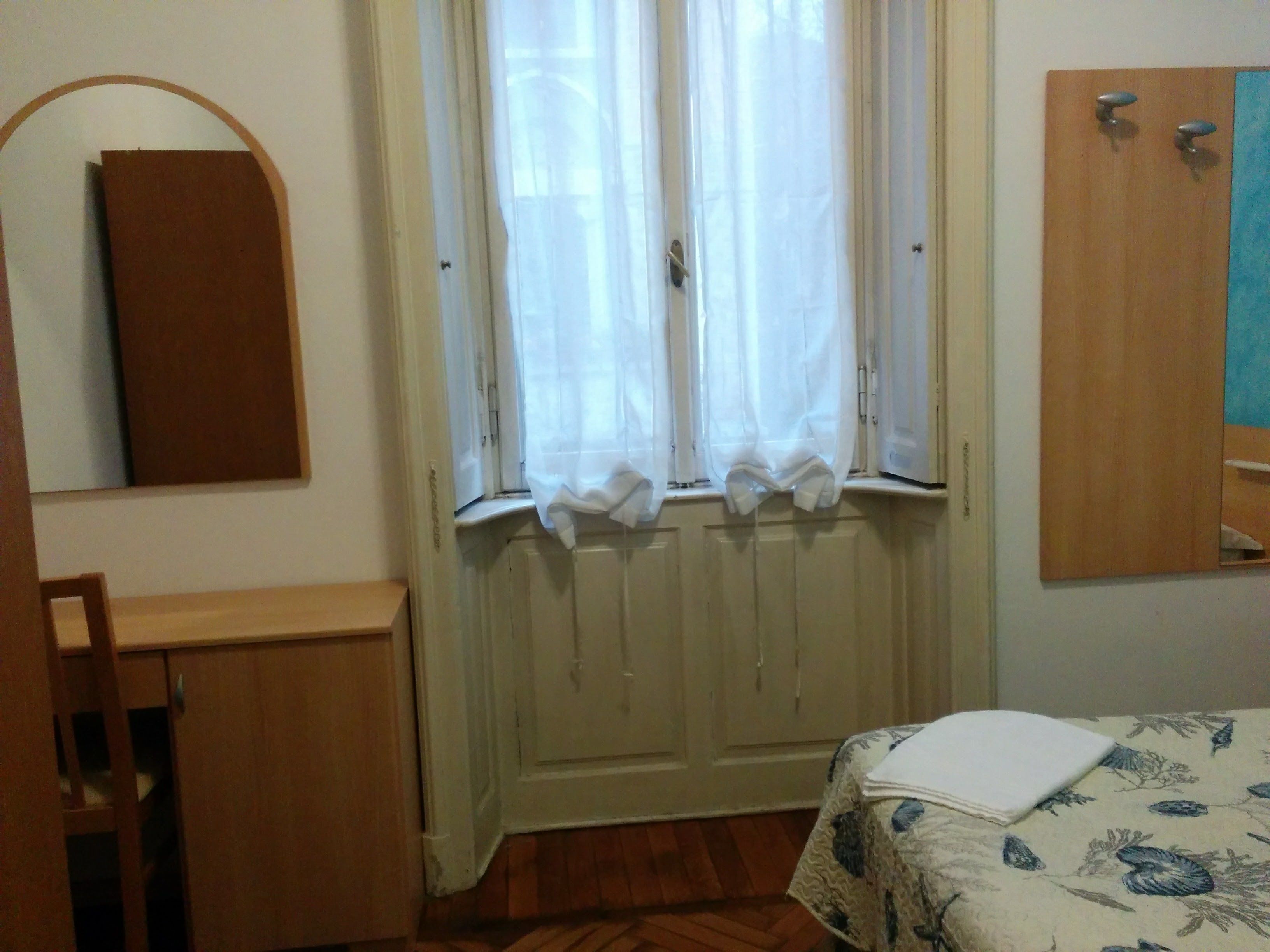Ein Schlafzimmer mit einem Holzbett, einem kleinen Nachttisch, einem Spiegel und einem Fenster mit Vorhängen.