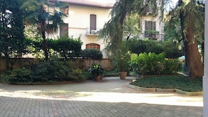 Une cour avec un chemin pavé, entourée d’une végétation luxuriante et bordée d’un bâtiment dont le toit est recouvert de tuiles.