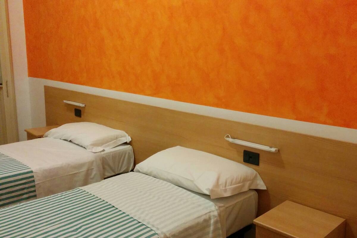 Quarto de hotel com duas camas de solteiro, cada uma com uma almofada e mesa de cabeceira.