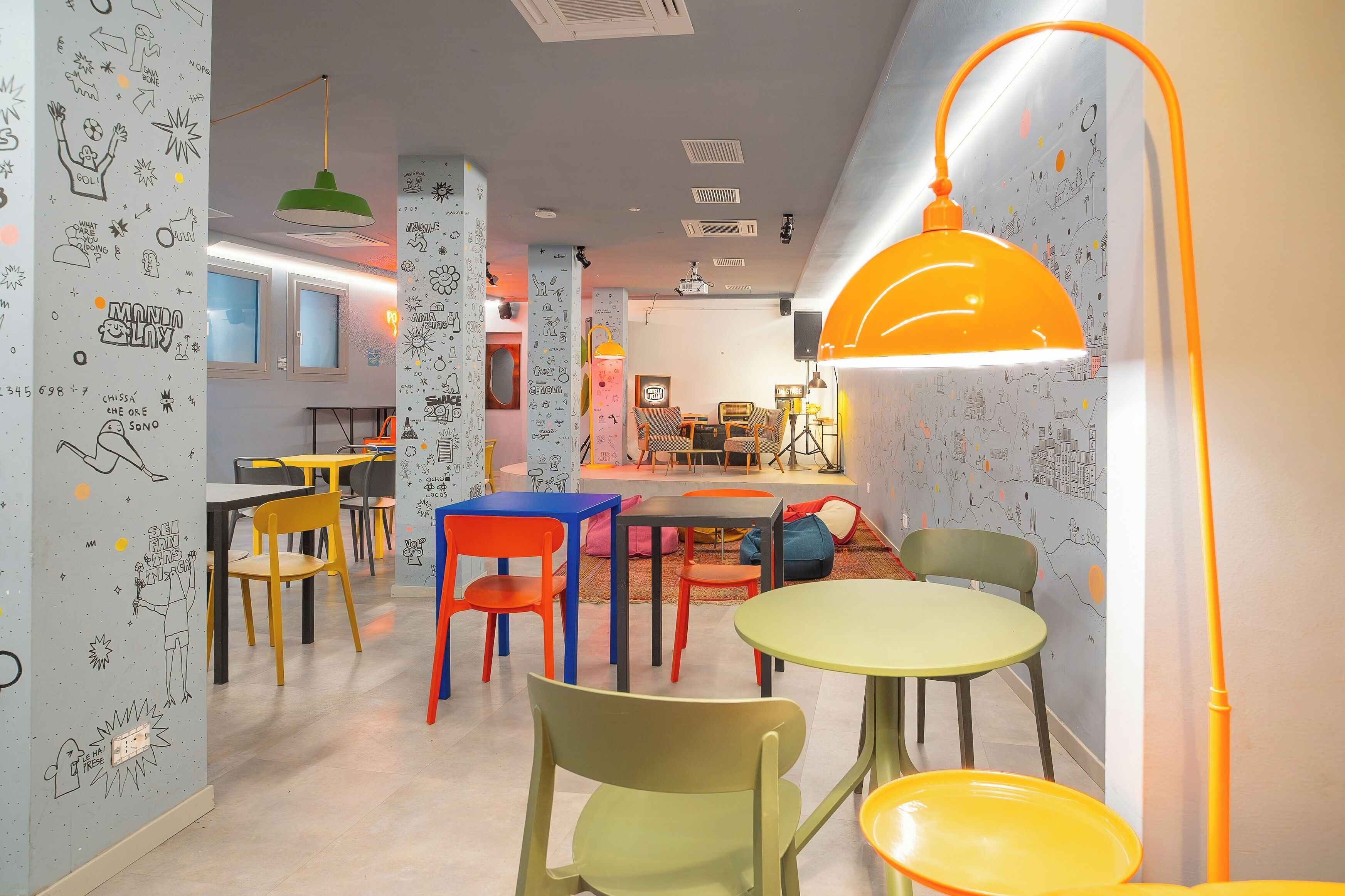 Una habitación con sillas coloridas, mesas y una lámpara naranja brillante.