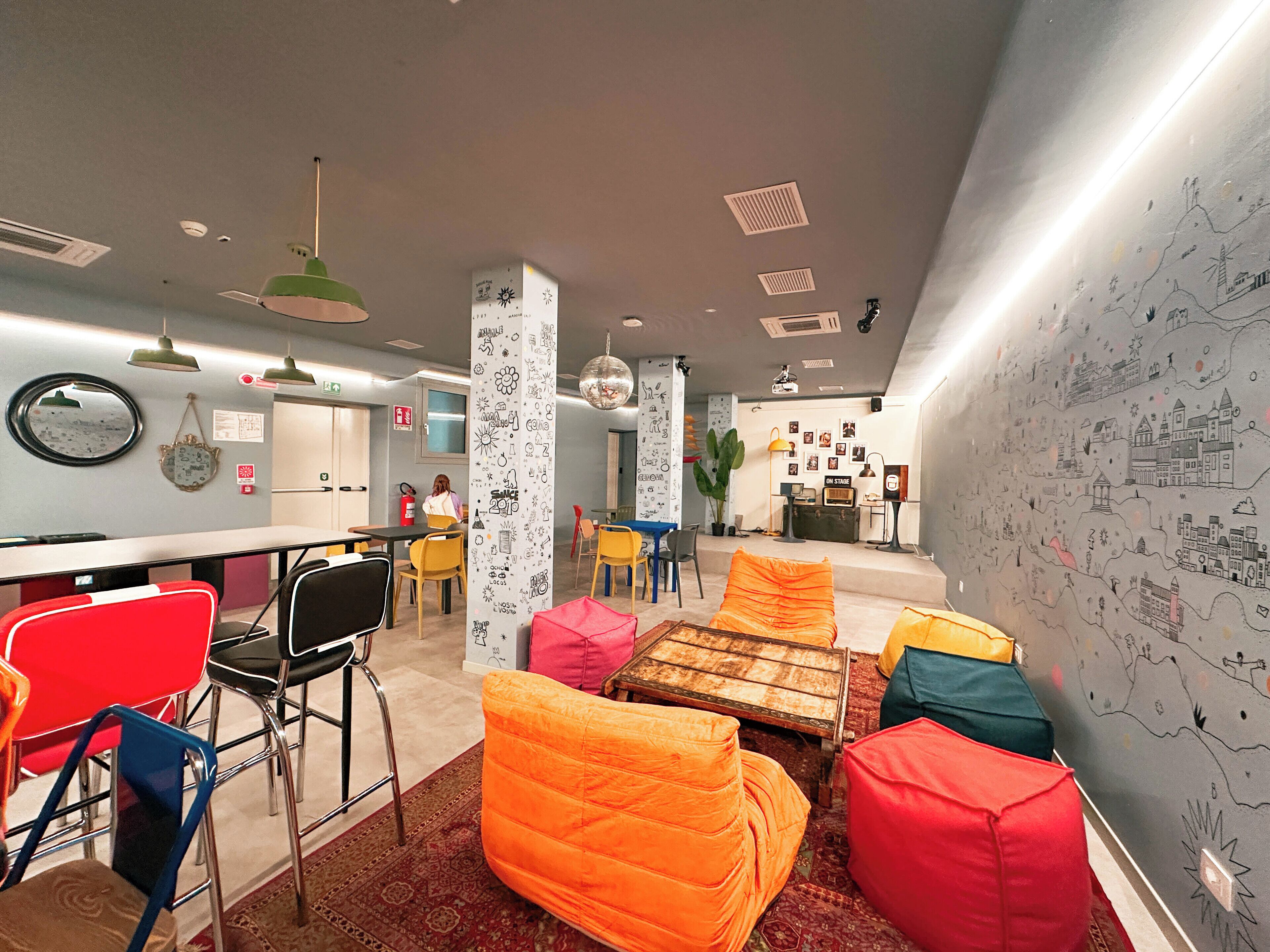 Un espace lounge moderne avec des sièges aux couleurs vives, un bar et un mur décoré de dessins.