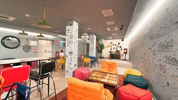 Un espace lounge moderne avec des sièges aux couleurs vives, un bar et un mur décoré de dessins.
