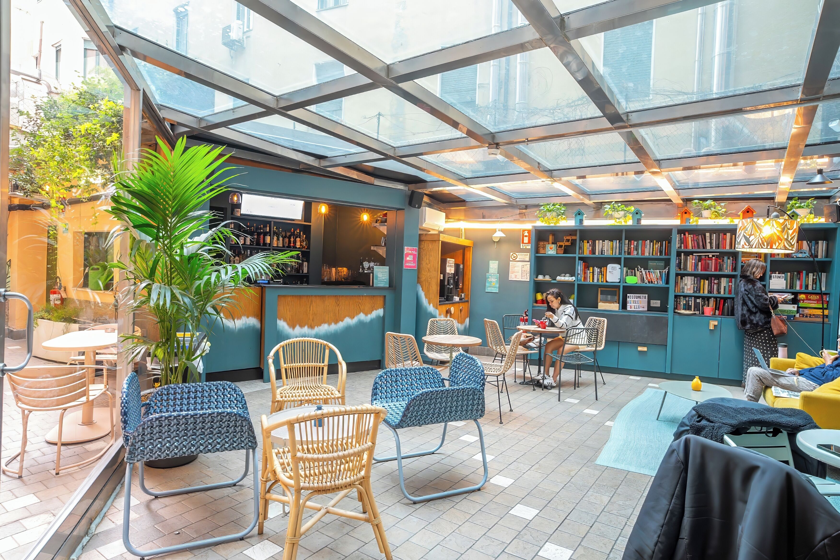 A café with a glass ceiling, wicker chairs, a bar area, and a bookshelf.