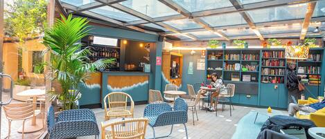 A café with a glass ceiling, wicker chairs, a bar area, and a bookshelf.