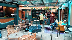 A cozy indoor cafe with a variety of seating options, including wicker chairs and tables, and a bar area with a counter and shelves of bottles. - Ostello Bello Milano Duomo (Milan)