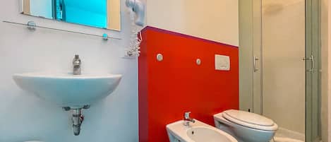 A bathroom with a white sink, bidet, and toilet, a mirror, and a shower area.
