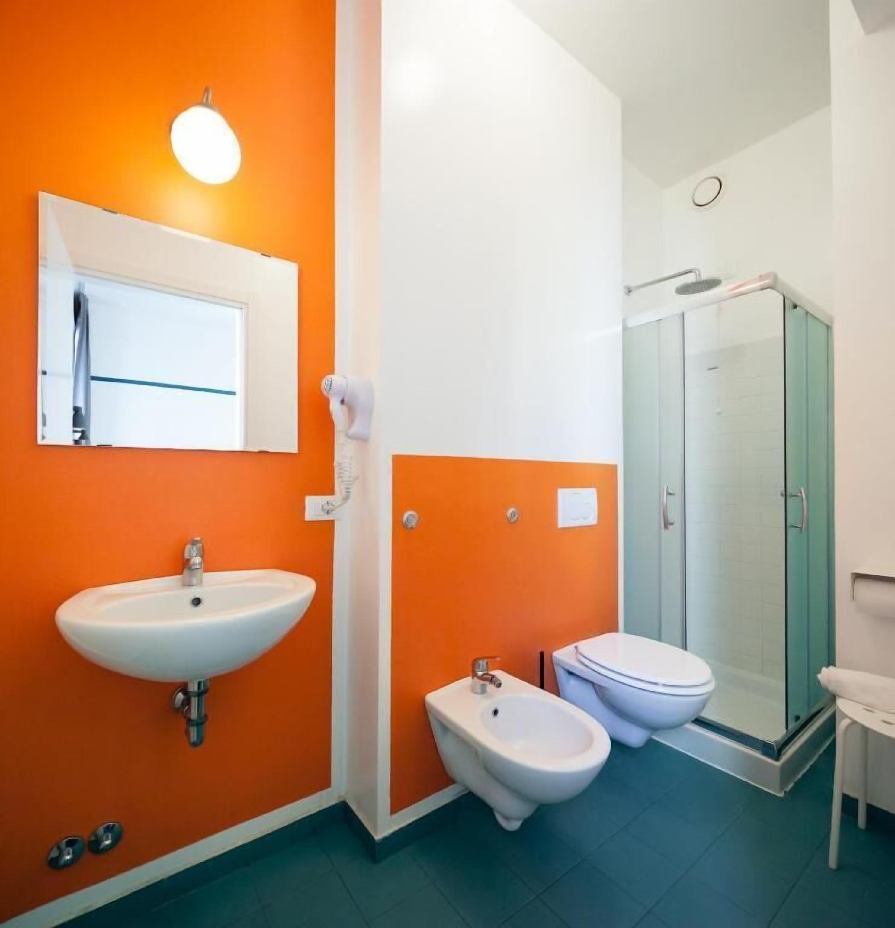 Ein Badezimmer mit einem weißen Waschbecken, zwei Bidets, einer Toilette und einer Duschkabine aus Glas.