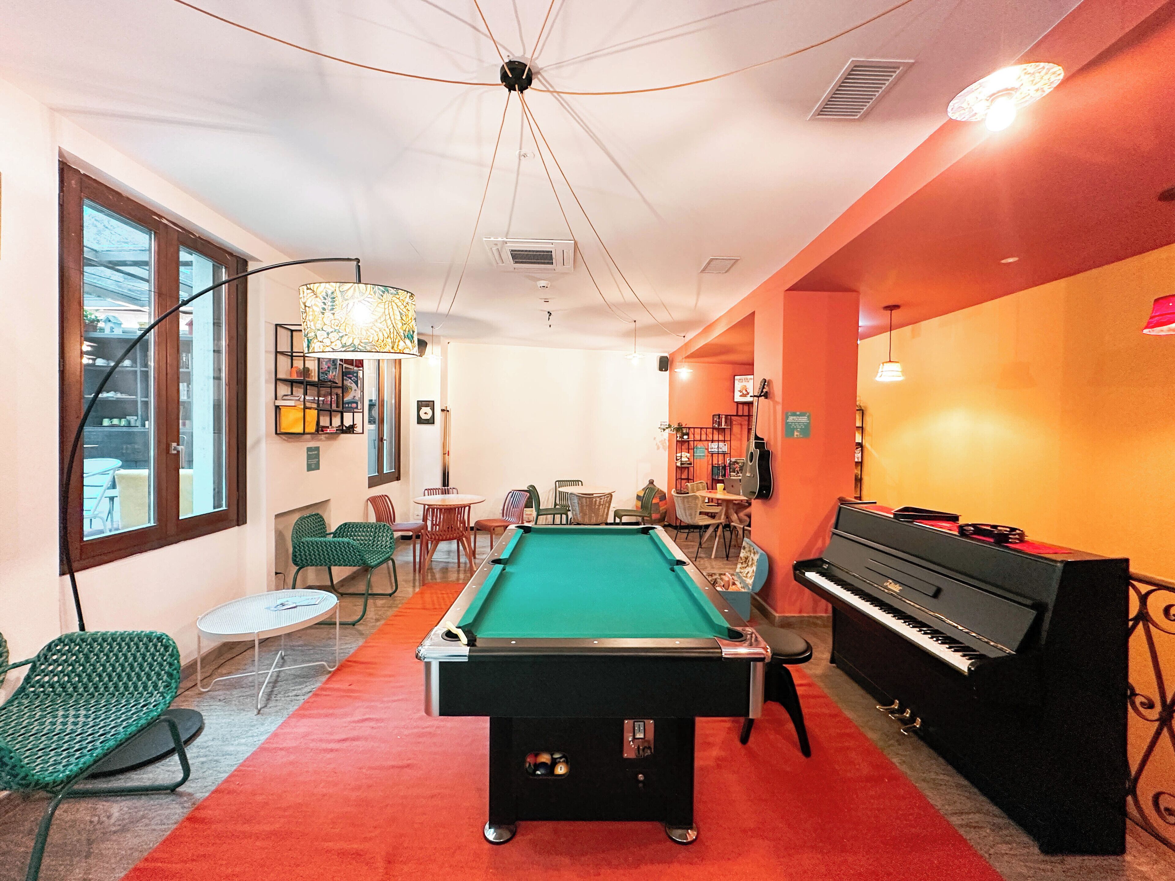 Une table de billard dans une pièce où se trouvent un piano, des chaises et une grande fenêtre.